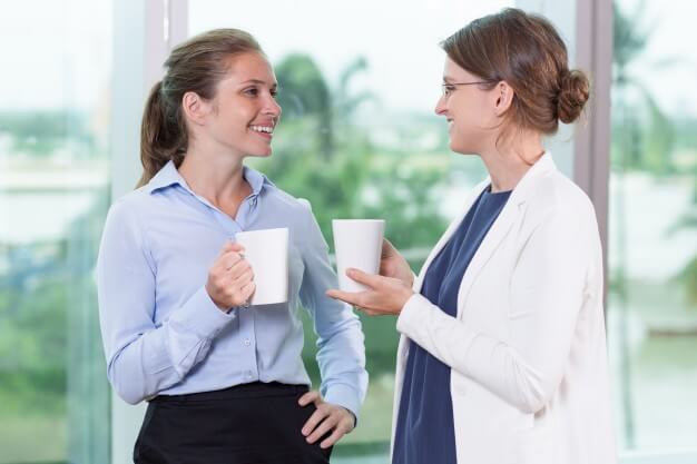 two smiling women drinking tea and speaking in office