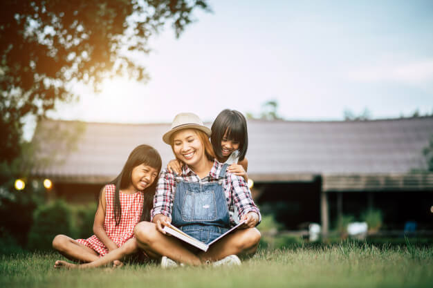 woman reading story to young daughters in garden