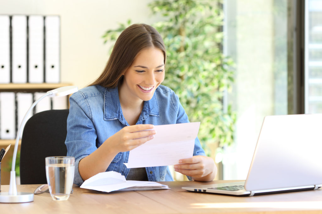 Young smiling businesswoman reading a direct mail letter at desk